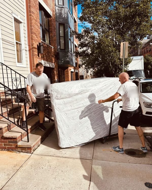 Two of our movers walking a plastic-wrapped mattress down a front stoop